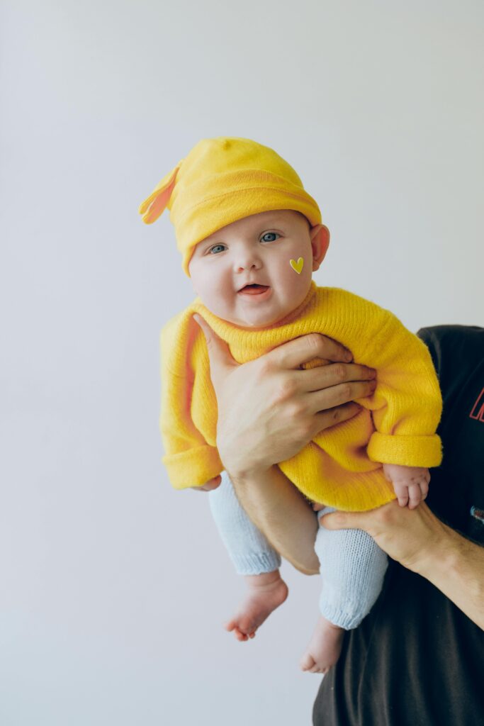pexels-photo-3845495-3845495-1 Cute baby in a yellow outfit being held indoors against a light background.